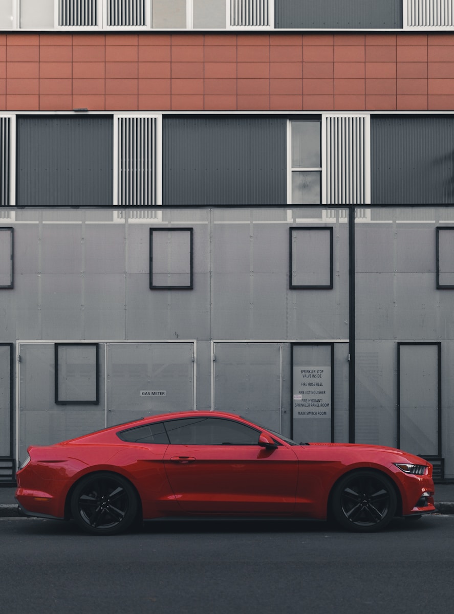 auto insurance red Ford Mustang coupe parked beside the building